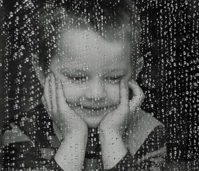little kid who is standing behind a window watching the rain