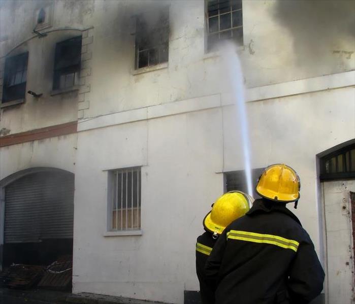 Two firefighters with a hose shooting water at a building on fire